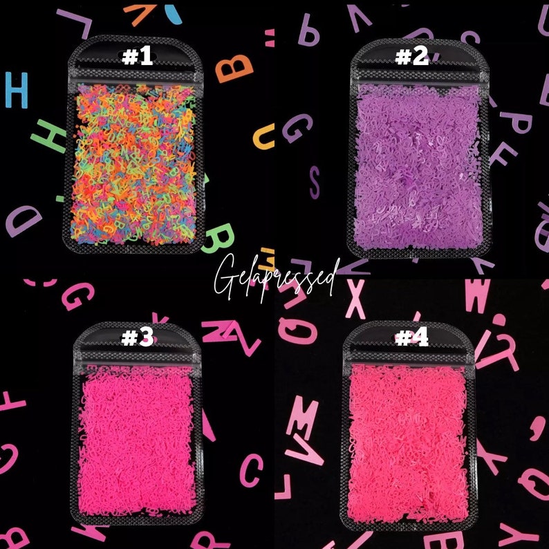 May include: Four small, clear bags filled with colorful alphabet-shaped sprinkles. The bags are labeled #1 through #4. The background is black with scattered letters in various colors. The text "Gelapressed" is in the center.