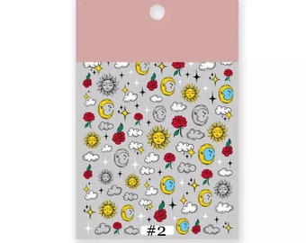 May include: A sheet of nail art stickers with a celestial theme. The stickers feature suns, moons, stars, clouds, and roses in yellow, red, and white on a gray background. The number "#2" is printed at the bottom.