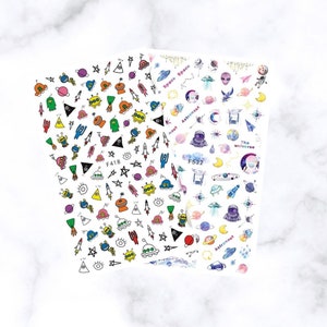 May include: Two sheets of nail art stickers featuring colorful space-themed designs. The stickers include aliens, rockets, planets, stars, and the words "Space" and "Astronaut". One sheet is labeled "F418" and the other "F532".