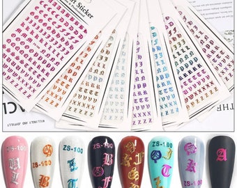 May include: Nail art stickers featuring gothic-style alphabet letters in various colors, including pink, orange, and purple. The image also shows several manicured nails with the same letter designs applied, showcasing the product's use. The stickers are labeled "Nail Art Sticker".