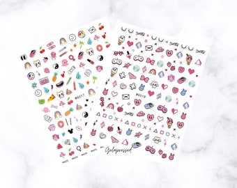 May include: Two sheets of nail art stickers with various colorful designs. One sheet features a variety of small illustrations including a rainbow, cherries, and a tooth. The other sheet has hearts, ice cream cones, and game controllers. The text "Gelapressed" is visible.