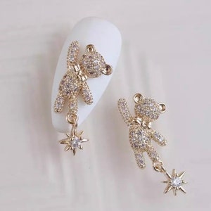 K&ouml;nnte beinhalten: Zwei goldfarbene B&auml;ren-Charms, besetzt mit klaren Kristallen. Jeder B&auml;r hat eine Fliege und einen baumelnden sternf&ouml;rmigen Charm mit einem einzelnen Kristall. Die Charms sind f&uuml;r Nailart konzipiert.