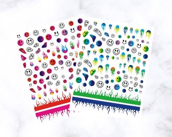 May include: Two sheets of colorful nail art stickers. One sheet has a red and pink flame design at the bottom, the other has a green and blue flame design. Both sheets have smiley faces, flames, and abstract shapes.