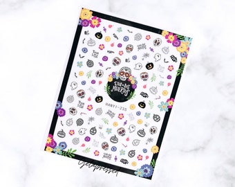 May include: A sheet of nail art stickers with a Day of the Dead theme. The stickers feature sugar skulls, pumpkins, ghosts, and flowers in various colors. The sheet has a black border and the text "Dia de los Muertos".