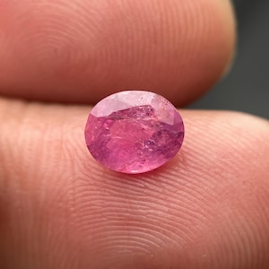Puede incluir: Una piedra preciosa ovalada de color rosa con un corte facetado. La piedra preciosa está colocada sobre un fondo rosa.