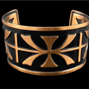 May include: A copper bracelet with a black background and a repeating pattern of stylized crosses.