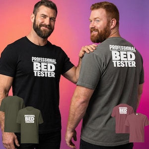 Könnte beinhalten: Zwei Männer tragen schwarze und graue T-Shirts mit dem Text "PROFESSIONAL BED TESTER" auf der Vorder- und Rückseite. Zusätzliche T-Shirts in Olivgrün und Burgunderrot werden darunter angezeigt. Der Hintergrund ist ein Farbverlauf aus Rosa, Orange und Lila.