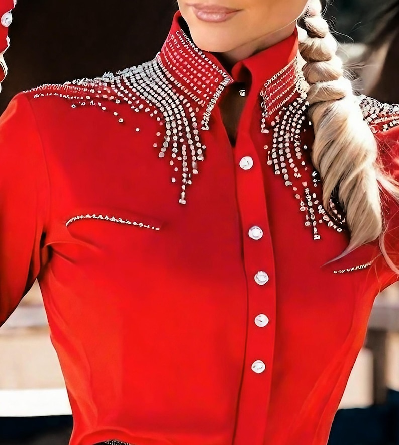 May include: A vibrant red button-down shirt with a high collar and long sleeves. The collar and shoulders are embellished with sparkling silver rhinestones. The shirt has white buttons and a tailored fit, suitable for equestrian or western wear.