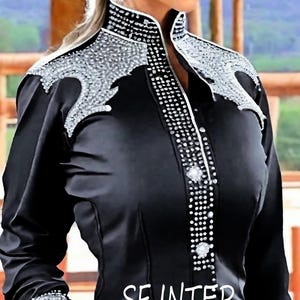 May include: A black long-sleeved shirt with a high collar and a silver rhinestone design. The shirt has a button-up front and a silver rhinestone trim around the collar.