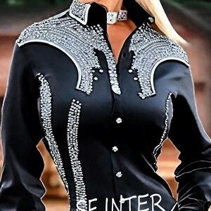 May include: A black long-sleeved shirt with a silver rhinestone design. The shirt has a pointed collar and a button-up front.