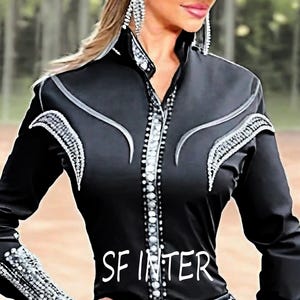 May include: A black long-sleeved shirt with silver embellishments and a silver trim around the collar and cuffs. The shirt has a button-up front and a curved design on the front. The text "SFINTER" is printed on the front of the shirt.