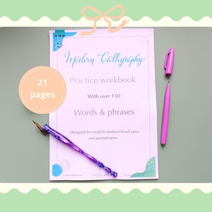 May include: A modern calligraphy practice workbook with 21 pages and over 150 words and phrases. The workbook is designed for small to medium brush pens and pointed pens. A purple pen and a pink pen are also in the image.