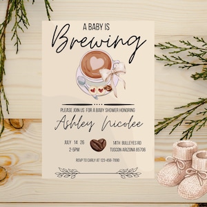 Pode incluir: Convite para chá de bebé com o texto "A Baby is Brewing" e um desenho de chávena de café. O convite inclui detalhes para o chá de bebé de Ashley Nicolee, com data, hora e local. Dois pares de botinhas de bebé estão no canto inferior direito.