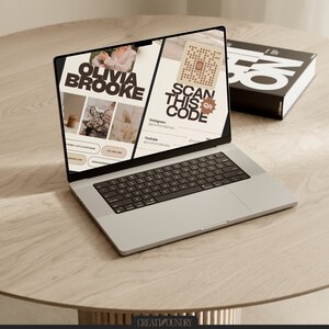 May include: A laptop computer open to a website with the text "Olivia Brooke" and "Scan this QR code". The website has a light brown background with images of a woman, a coffee cup, and a plant. The laptop is on a light brown wooden table.