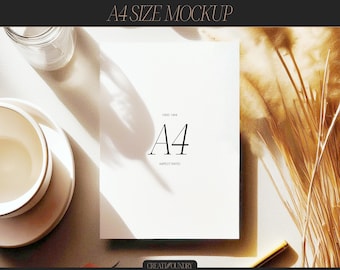 Puede incluir: Una maqueta de papel blanco de tamaño A4 con el texto "A4" y "ASPECT RATIO" sobre una superficie beige claro con flores secas y una taza y un platillo de cerámica blanca.