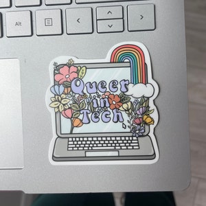 May include: A sticker with a laptop computer surrounded by flowers and a rainbow. The laptop screen says "Queer in Tech".