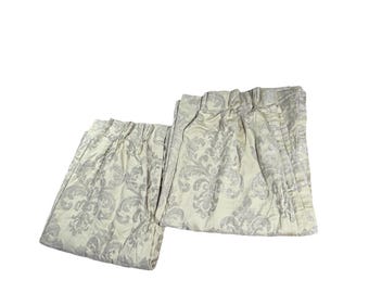 May include: Two light-colored curtain panels with a gray floral pattern. The curtains are folded and appear to be made of a textured fabric. The design is a classic damask style, suitable for home decor.