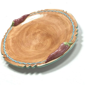 Puede incluir: Un plato de servir redondo de cerámica con un esmalte marrón y un borde festoneado azul y verde. Dos chiles rojos están unidos al borde del plato.