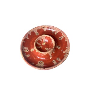 May include: A red ceramic serving dish with a smaller, round dish in the center. The dish has a speckled glaze with a light brown and white pattern.