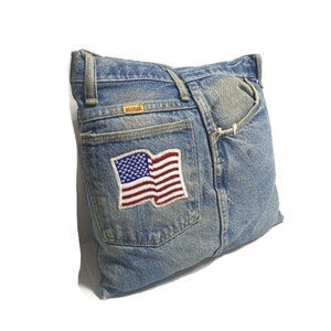 Op de afbeelding: Een blauw denim kussen met een achterzak en een Amerikaanse vlag patch. De zak heeft een "RUSTLER" label.