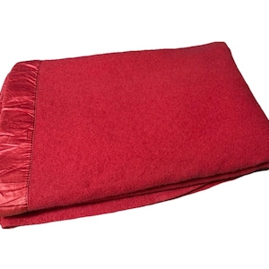 Pode incluir: Um cobertor vermelho dobrado com uma borda de cetim. O cobertor é de cor sólida e parece ser feito de um material macio. A borda de cetim adiciona um toque de elegância ao cobertor.