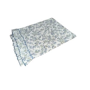 May include: A rectangular white blanket featuring a repeating pattern of small blue flowers and green leaves. The blanket is finished with a ruffled edge detail along one side, accented by a thin blue trim that separates the ruffle from the main body.