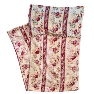 May include: A floral patterned fabric with vertical stripes in cream, burgundy, and pink. The fabric features a repeating pattern of flowers and leaves. The top edge has a decorative trim. The fabric is folded.