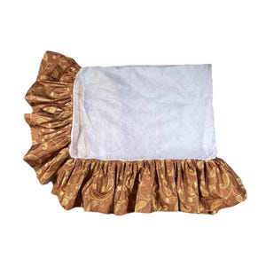 Puede incluir: Una almohada rectangular con un centro blanco y un borde con volantes. El borde es de color marrón intenso con un estampado de cachemira dorado. La almohada está diseñada para ropa de cama.