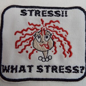 May include: White embroidered patch with a cartoon woman with red hair and the text "STRESS!! WHAT STRESS?"