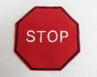 Könnte beinhalten: Rotes achteckiges Stoppschild mit weiß gesticktem Text "STOP".