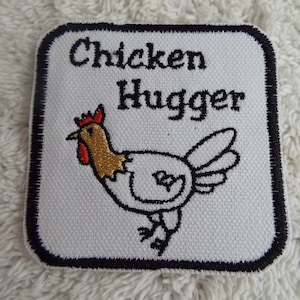May include: Square patch with the words "Chicken Hugger" above a cartoon chicken. The chicken is white with a gold neck and red comb. The patch has a black border and is on a white textured background.
