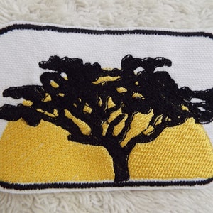 Puede incluir: Parche bordado negro con una silueta de un árbol frente a un sol amarillo. El parche tiene un fondo blanco y un borde negro.