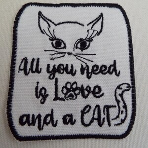 May include: White embroidered patch with black stitching. The patch features a cartoon cat with the text "All you need is Love and a CAT".