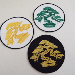 May include: Three embroidered patches featuring bonsai tree designs. One patch has a gold tree on a black background, another has a green tree on white, and the third has a gold tree on white. Each patch is circular with a black border.