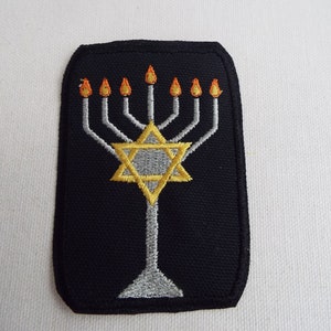 May include: A black embroidered patch with a silver menorah and a gold Star of David. The menorah has seven candles with orange flames.