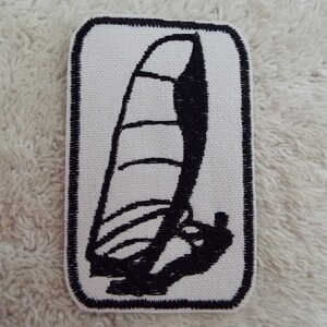 Puede incluir: Parche bordado en blanco y negro de un velero con una vela. El parche es rectangular y tiene un fondo blanco con un borde negro.
