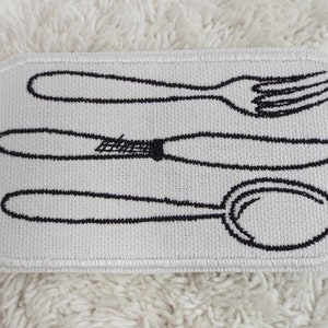 Può includere: Toppa di tessuto bianco con immagini ricamate in nero di una forchetta, un coltello e un cucchiaio.