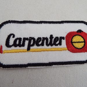 May include: White embroidered patch with a black outline. The patch features a yellow and red measuring tape with the word "Carpenter" in black lettering.