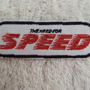 May include: White embroidered patch with black border. The text "The Need For Speed" is in black and the word "SPEED" is in red with a stylized motion blur effect.