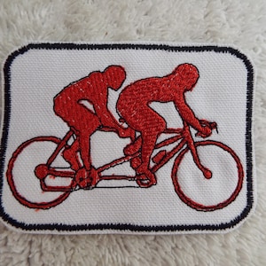 Peut inclure: Patch brodé rouge représentant deux personnes à vélo en tandem. Le patch est bordé de noir.