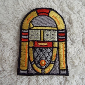 Puede incluir: Parche bordado para planchar de una máquina de discos vintage con detalles rojos, amarillos y grises.