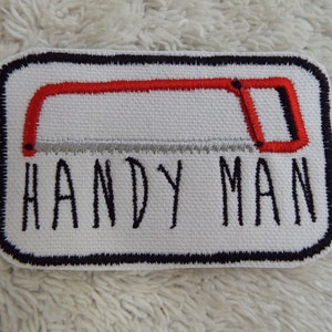 Peut inclure: Patch brodé blanc avec une lame de scie rouge et le texte "HANDY MAN" en noir.