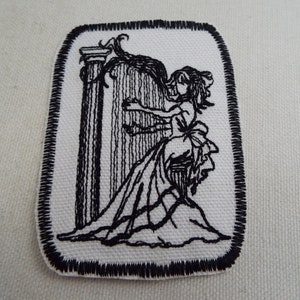 May include: Black and white embroidered patch of a woman playing a harp. The patch is rectangular with a black stitched border.