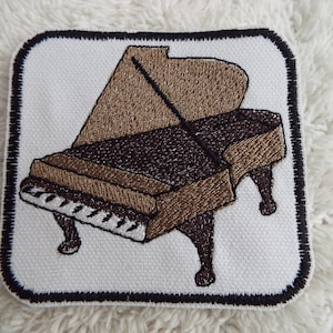 May include: Embroidered patch of a brown grand piano with a black interior and white keys. The patch is surrounded by a black border.