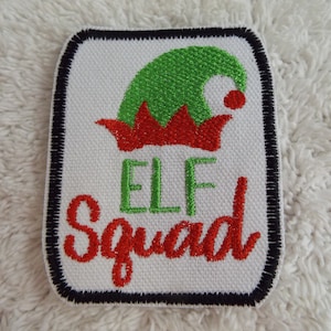 Könnte beinhalten: Weißer gestickter Bügel-Patch mit einer grünen Elfenmütze und rotem Besatz. Der Text "ELF Squad" ist in Rot und Grün gestickt.