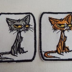 May include: Two embroidered iron-on patches featuring cartoon cats with grumpy expressions. The cat on the left is gray and the cat on the right is orange.