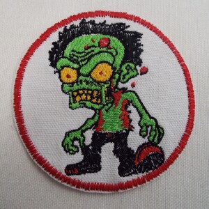 May include: A green zombie cartoon character with red eyes and a red border around the image. The zombie is wearing black pants and has a red stain on its chest.