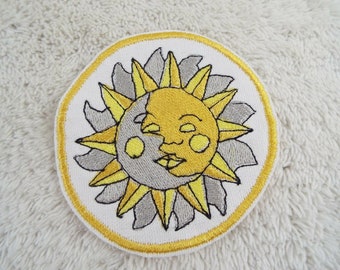 May include: A yellow and grey embroidered patch featuring a sun and moon design. The sun has a smiling face and the moon is crescent shaped.