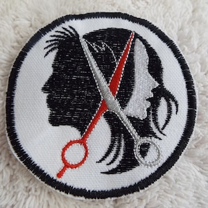 May include: A white embroidered patch with a black silhouette of a person's head with a pair of scissors crossing through the hair. One scissor blade is red and the other is silver.