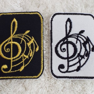 May include: Two embroidered iron-on patches featuring a treble clef with musical notes. One patch is black with gold embroidery, and the other is white with black embroidery.
